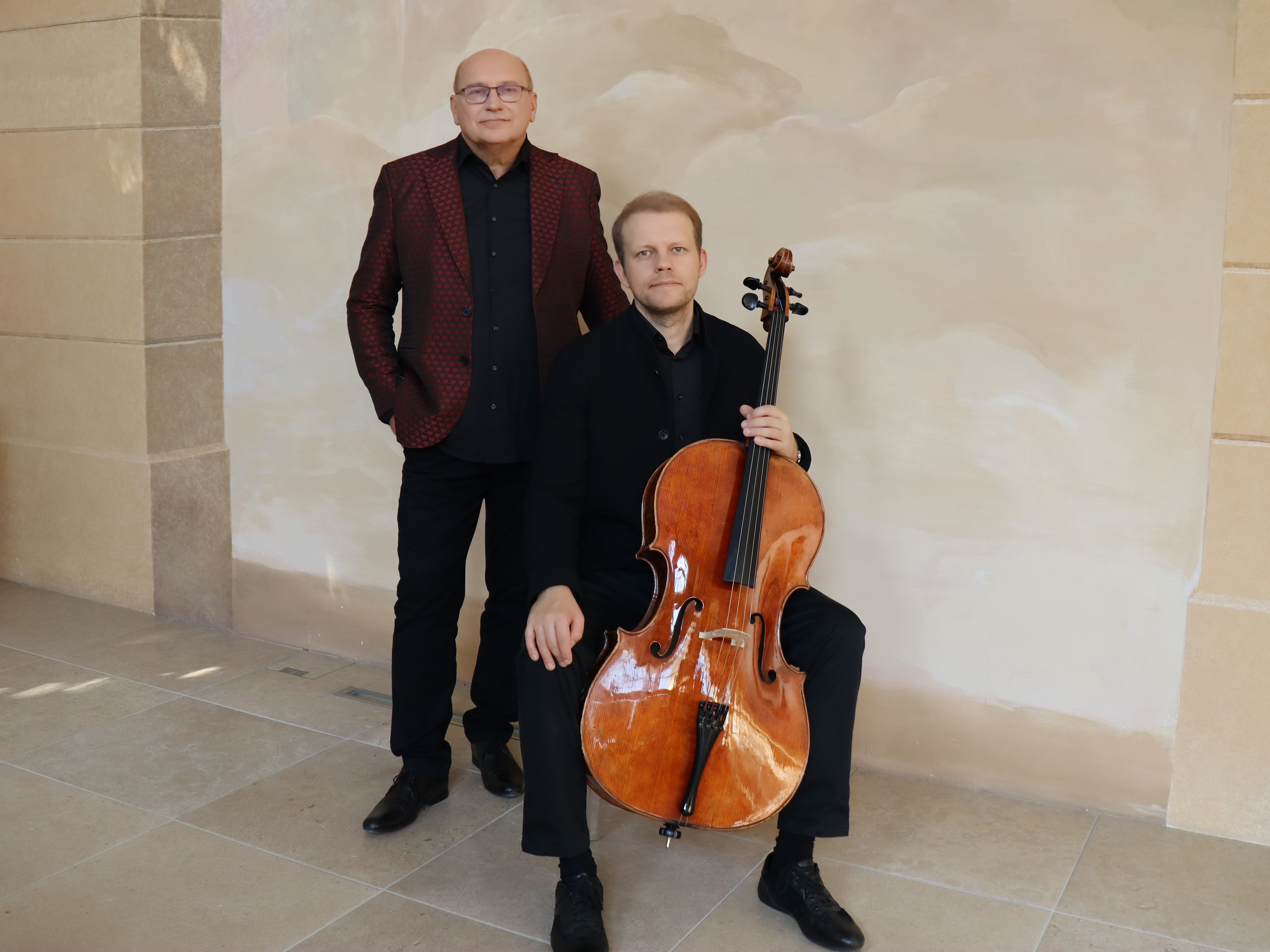 KI generiert: Zwei Männer posieren in elegantem Ambiente, einer sitzt mit einem Cello, der andere steht daneben. Das Bild vermittelt eine professionelle und musikalische Atmosphäre.