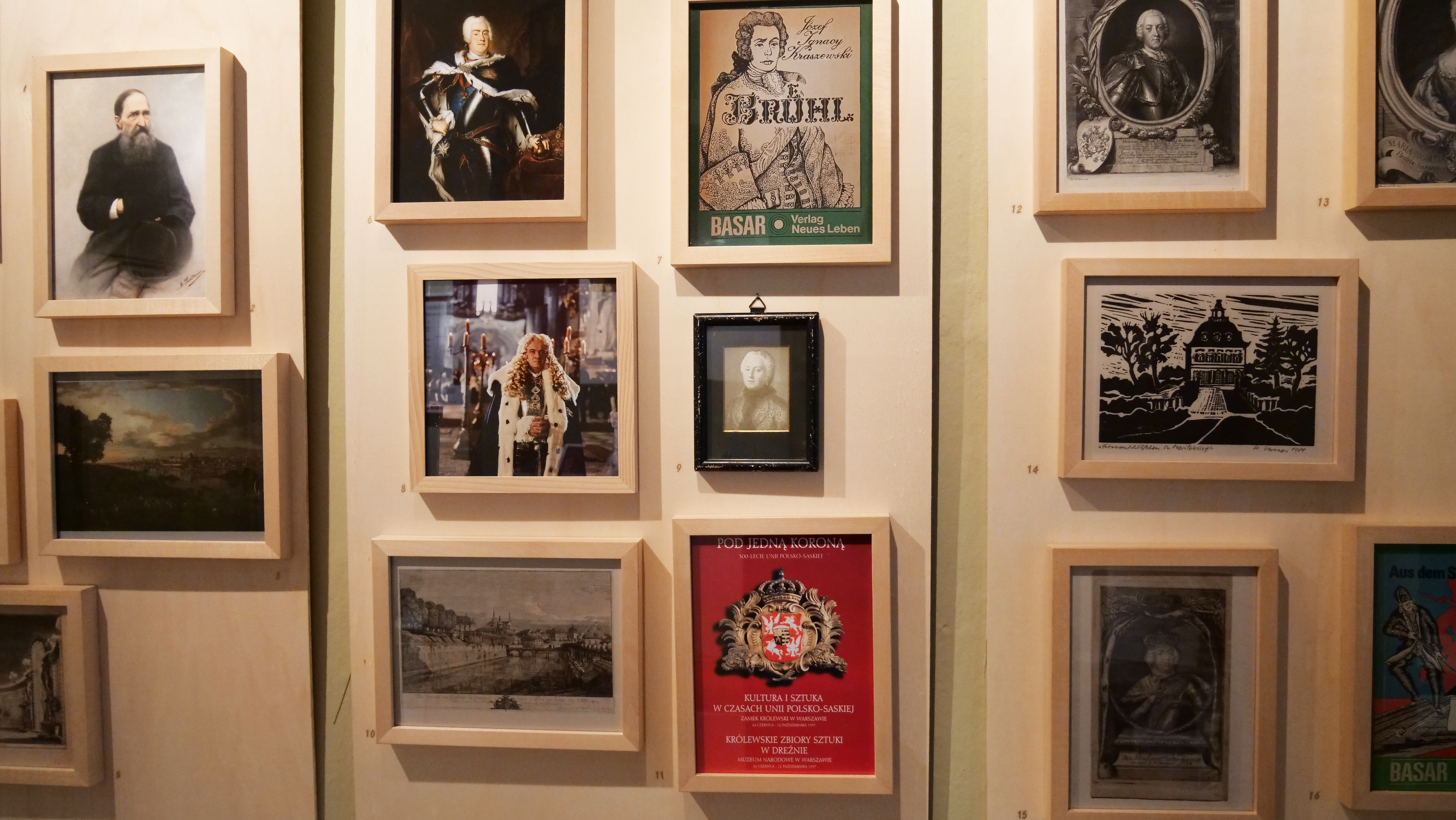 KI generiert: Das Bild zeigt eine Wand mit einer Sammlung von gerahmten Kunstwerken und Fotografien, die in einem Ausstellungsraum präsentiert werden. Die Motive umfassen Porträts, historische Szenen und Drucke.