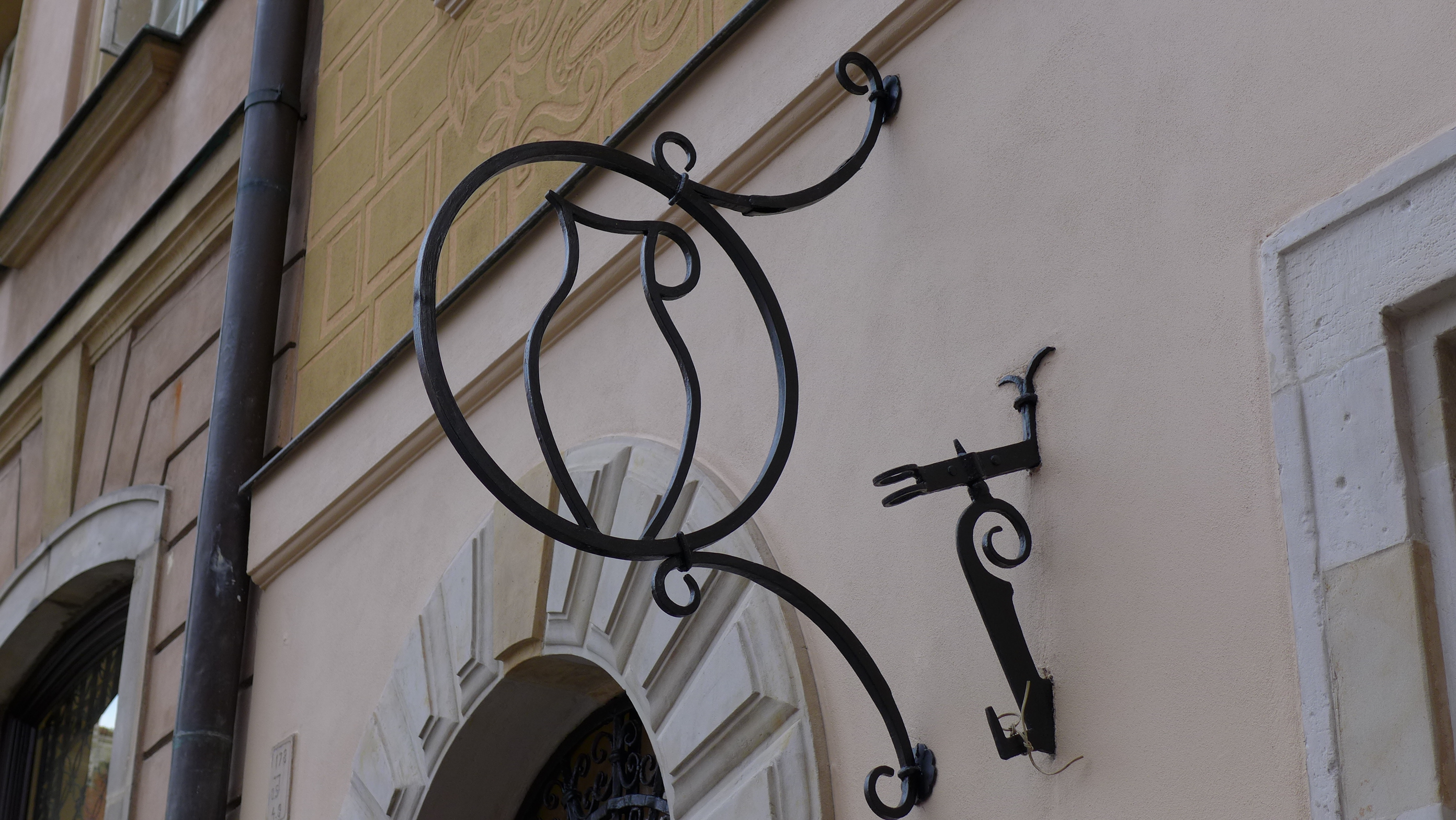 KI generiert: Das Bild zeigt ein kunstvoll gestaltetes, leider beschädigtes, altes Metallschild auf der Fassade eines Gebäudes. Das Schild ist leer, und der dekorative Metallrahmen ist noch vorhanden.