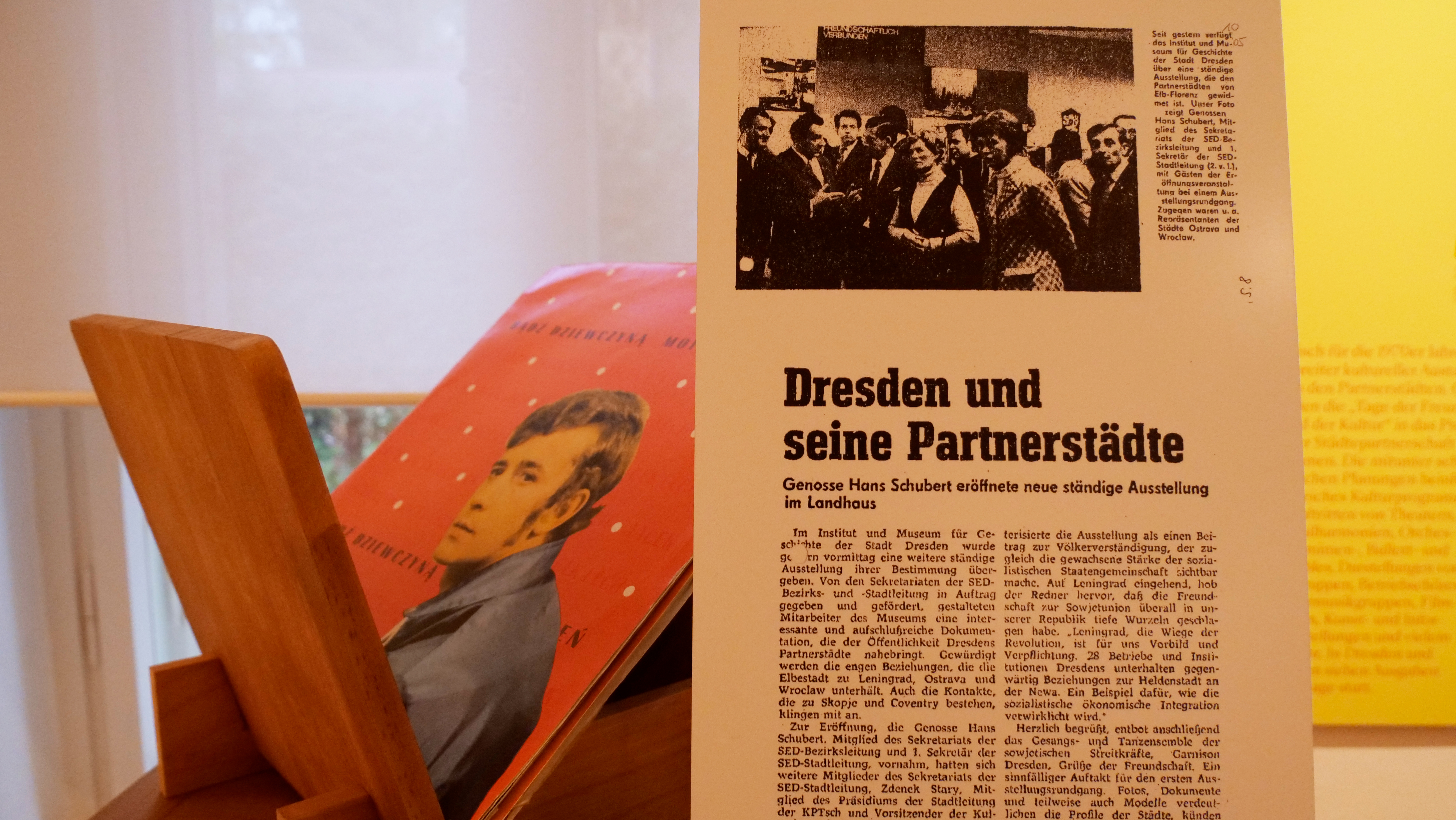 KI generiert: Das Bild zeigt einen Artikel mit dem Titel "Dresden und seine Partnerstädte" über eine Ausstellungseröffnung in London. Im Hintergrund ist ein weiteres Buch oder Magazin mit einem Porträt auf dem Cover zu sehen.