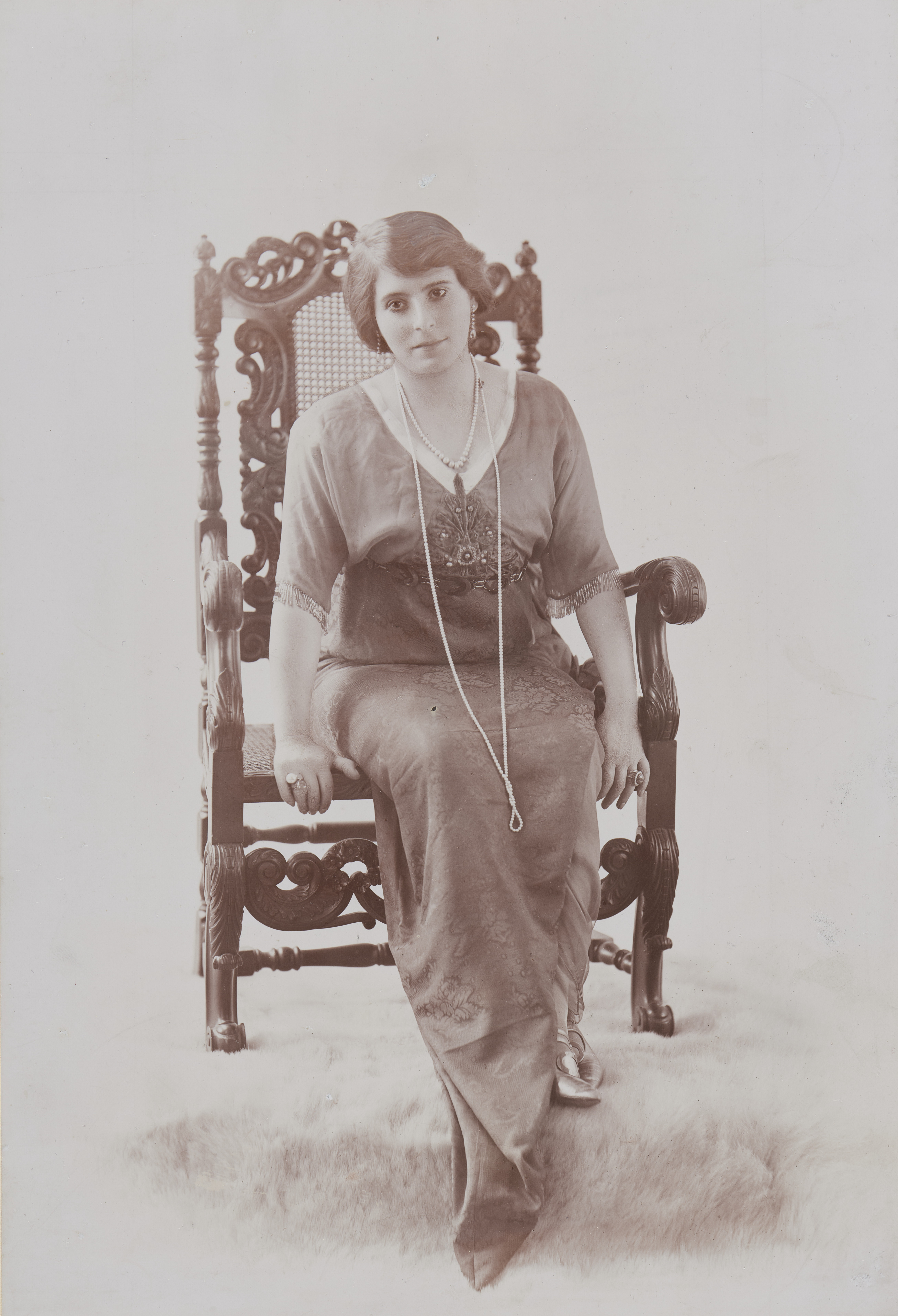 KI generiert: Das Bild zeigt eine Frau in einem historischen Porträt, gekleidet mit einem Hut und einem Umhang oder Schal, während sie zur Seite schaut. Sie hält einen kleinen Blumenstrauß in der Hand.