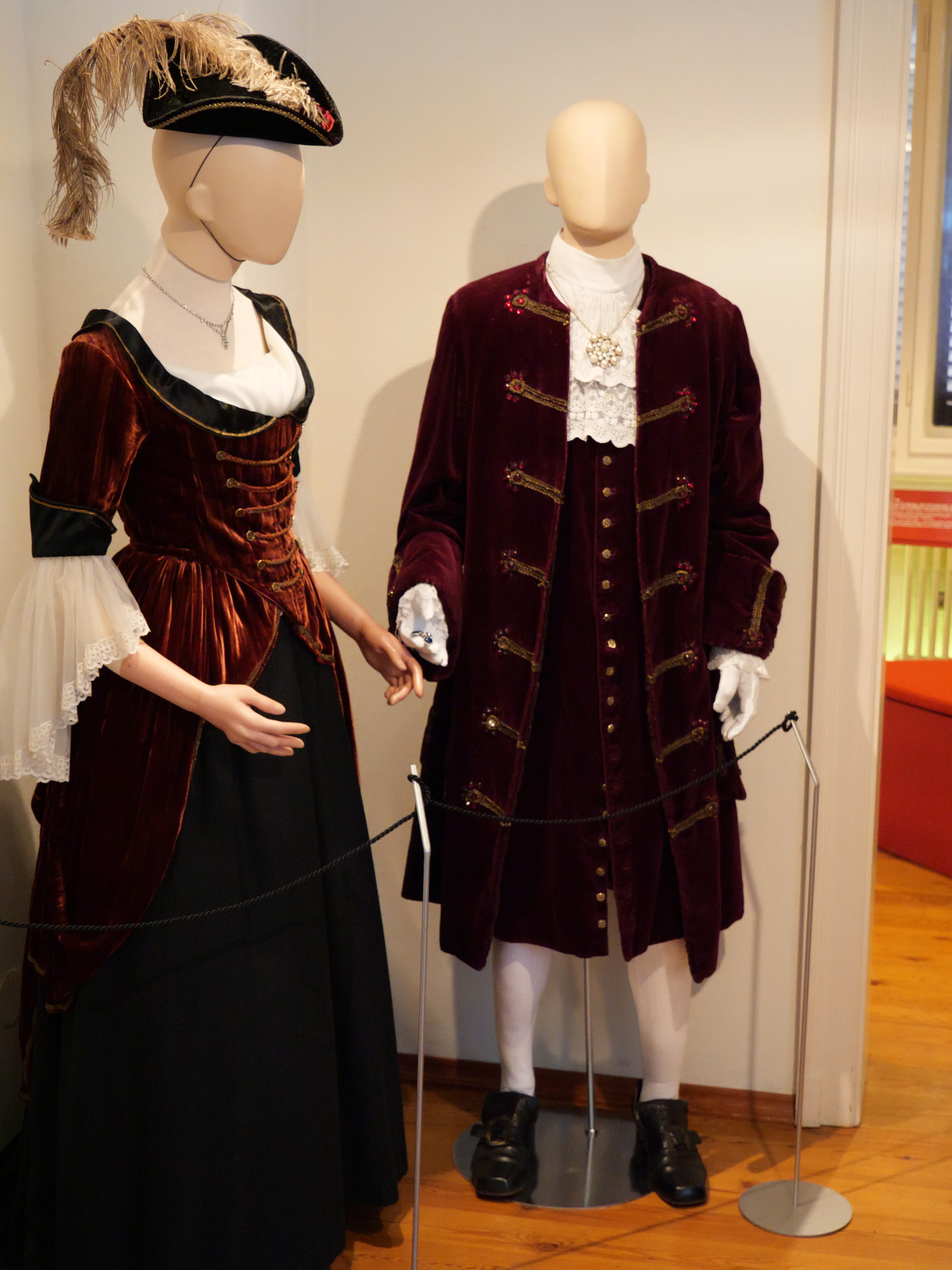 AI generated: The image shows two mannequins dressed in historical costumes, including a dress and a suit made of a red, velvet-like fabric. The clothes appear to be from an earlier era and are on display in an exhibition.